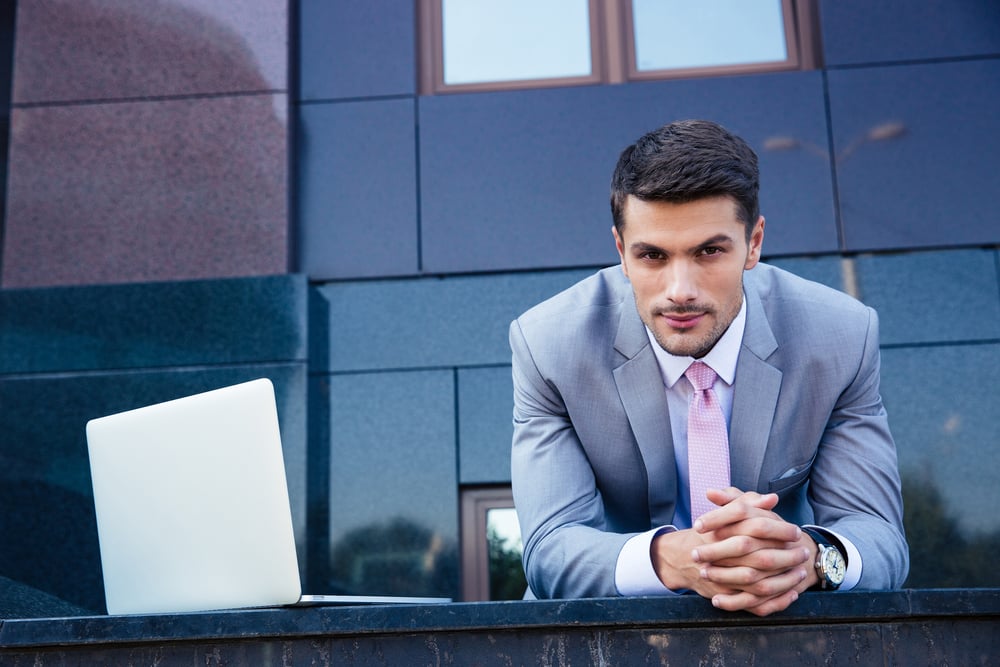 Portrait of a confident businessman with laptop computer outdoors. Looking at camera