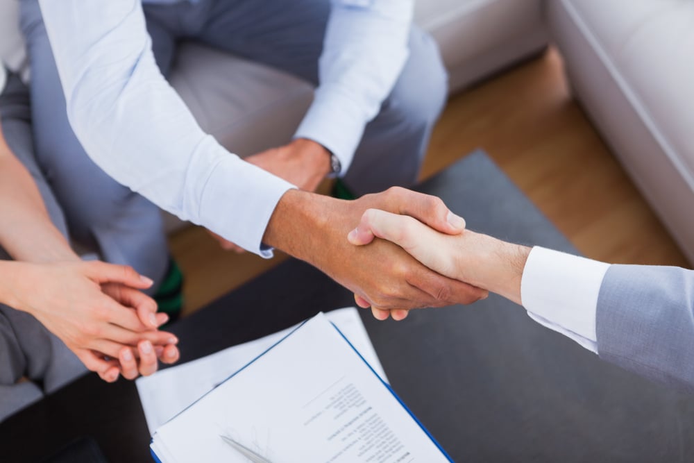Salesman shaking hands with client with contract on the coffee table