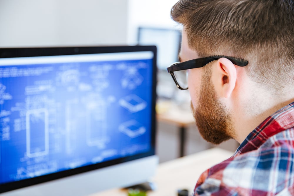 Closeup of young man in glasses with beard making blueprints on computer-2