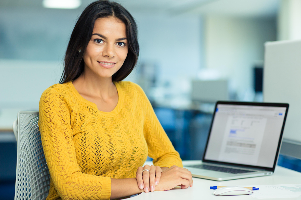 Portrait of a happy casual businesswoman in sweater sitting at her workplace in office